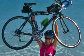 Lynn West Salvo ’71 hoists her bike over her head on the beach
